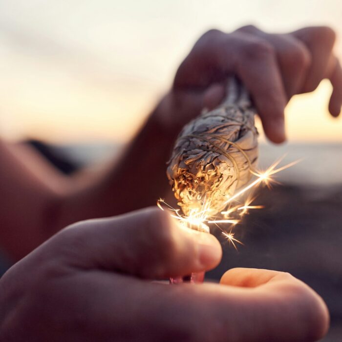 Hand, flame and sage burning at the beach for a spiritual ritual and meditation practice. Herb, fin