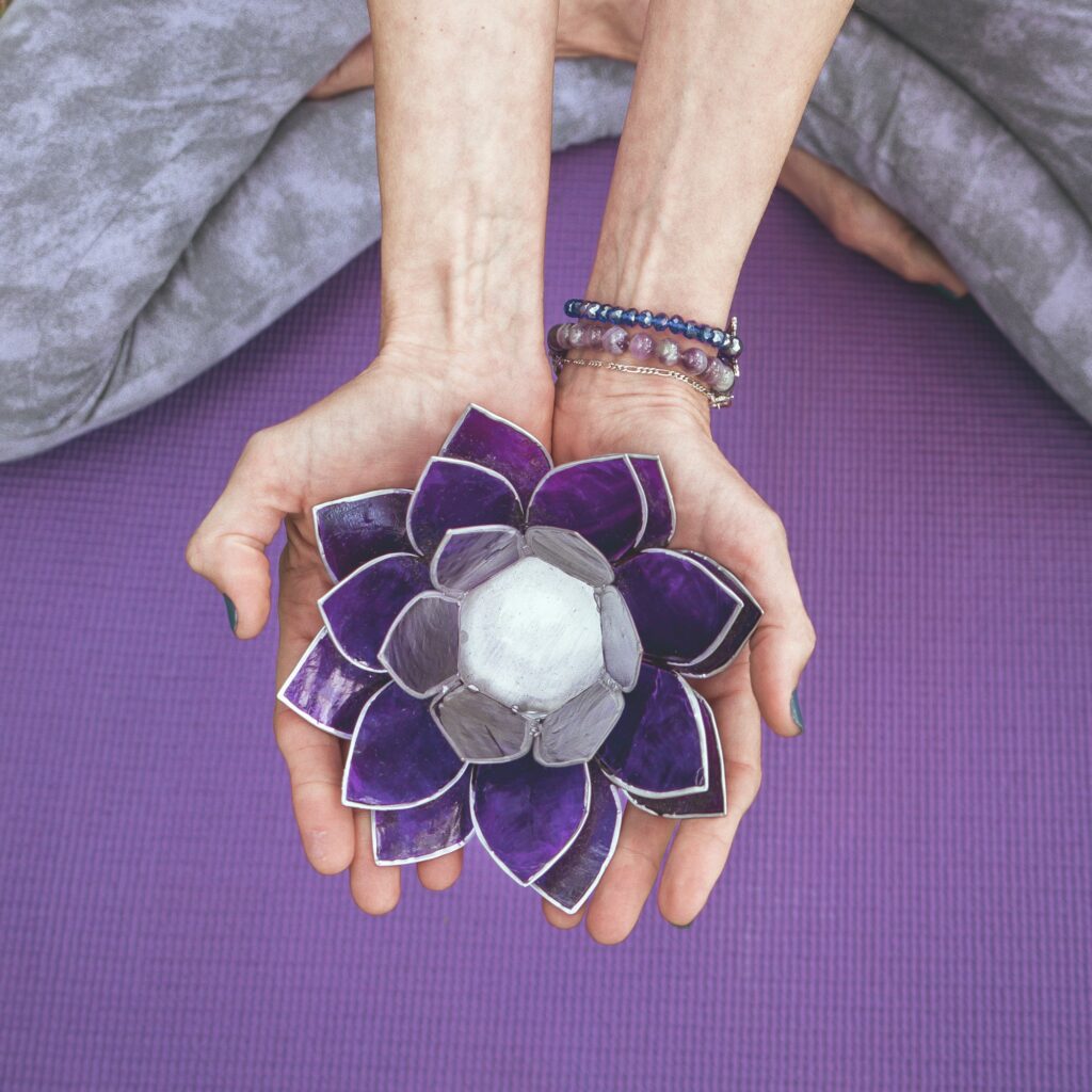 Top angle view of hands holding a purple glass lotus. Yoga and meditation concept.